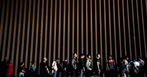 Varias personas se forman junto a un muro fronterizo mientras esperan para poder solicitar asilo luego de cruzar la frontera desde México, el 11 de julio de 2023, cerca de Yuma, Arizona. Foto: Gregory Bull, AP