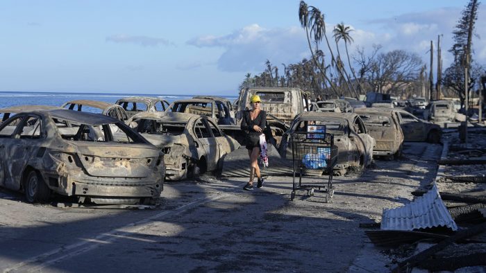 Una mujer camina entre los restos de vehículos consumidos por el fuego, el viernes 11 de agosto de 2023, en Lahaina, Hawai. 