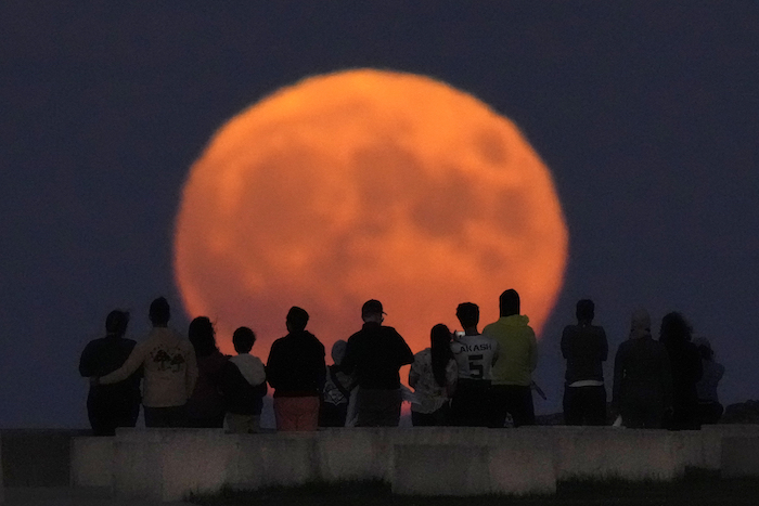 Una rara súperluna azul se levanta sobre el lago Michigan ante la mirada de los curiosos reunidos en un banco en la calle 31st, en Chicago, el 30 de agosto de 2023.