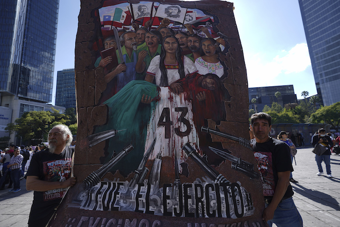 Dos hombres llevan una pancarta sobre los 43 estudiantes de Ayotzinapa mientras familiares y simpatizantes marchan por el noveno aniversario de su desaparición, en Ciudad de México, el martes 26 de septiembre de 2023.