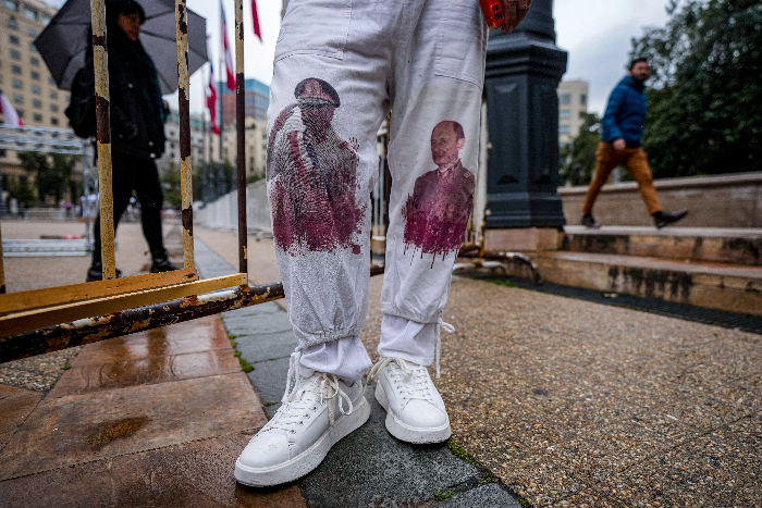 Hugo Toledo lleva pantalones con los retratos ensangrentados del fallecido dictador chileno Augusto Pinochet, izquierda, y el excomandante del ejército chileno Juan Cheyre, a quien considera responsable de su encarcelamiento y tortura al inicio de la dictadura en un evento que marca la victoria electoral del Presidente Salvador Allende en 1970, frente al palacio presidencial de La Moneda en Santiago, Chile, el lunes 4 de septiembre de 2023.