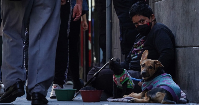 Una persona en situación precaria solicita un ayuda económica en calles del Centro Histórico para dar alimento a sus mascotas, un perro y un gato, que lucen abrigados por las bajas temperaturas.