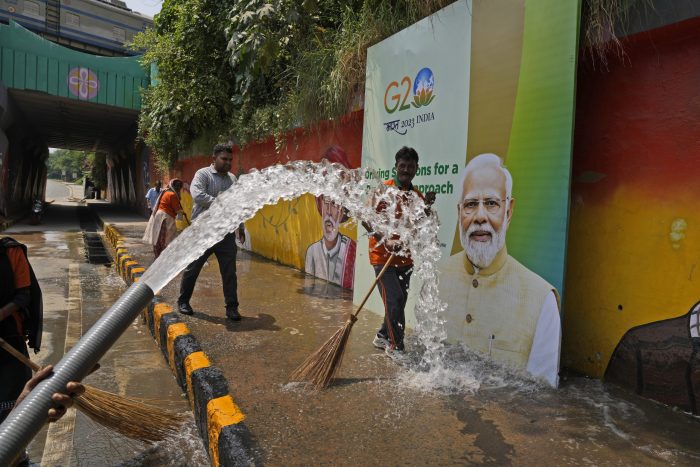 Trabajadores municipales lavan una acera junto a un cartel con la imagen del Primer Ministro indio Narendra Modi antes de la cumbre del Grupo de los Veinte a realizarse en su país esta semana, el jueves 7 de septiembre de 2023, en Nueva Delhi, India.