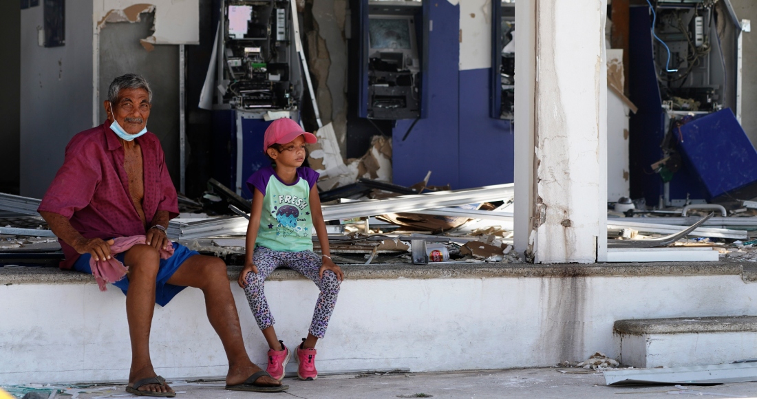 Residentes sentados delante de una entidad bancaria, sin ventanales y con los cajeros destrozados, dos días después del paso del devastador huracán Otis, de categoría cinco, en Acapulco, México, el viernes 27 de octubre de 2023.