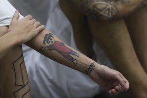 El brazo de un preso con un tatuaje en una clase de terapia social sobre comportamiento durante una visita de prensa en el Centro de Confinamiento del Terrorismo, una mega prisión en Tecololuca, El Salvador, el jueves 12 de octubre de 2023. Llevan mascarillas como precaución para evitar contagios de Covid-19. Foto: Salvador Meléndez, AP