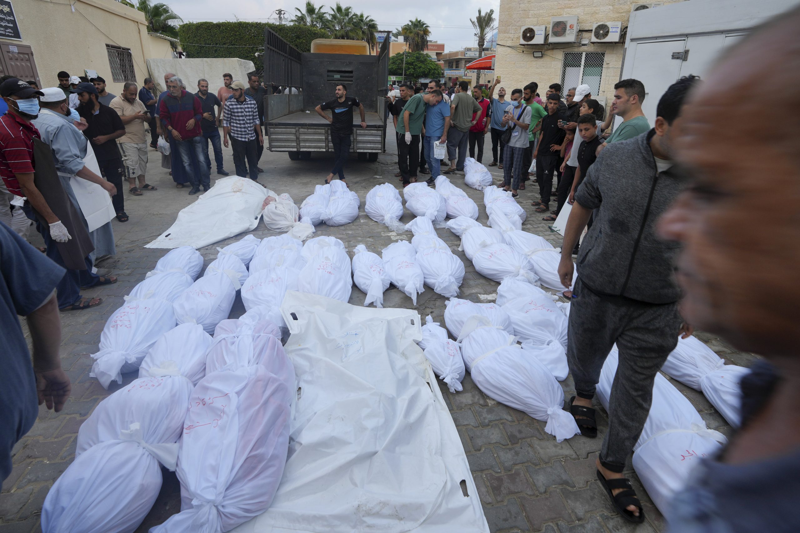 Palestinos de pie junto a cadáveres de personas que murieron por los bombardeos israelíes en la Franja de Gaza, frente a la morgue de Deir Al-Balah, el martes 24 de octubre de 2023. 