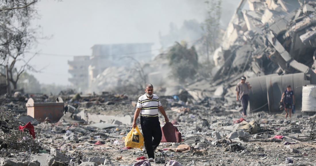 Algunos palestinos caminan junto a edificios destruidos tras un bombardeo israelí sobre Al Zahra, el viernes 20 de octubre de 2023, en las afueras de la Ciudad de Gaza.