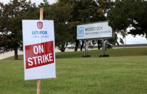 Un letrero de huelga, colocado por el sindicato Unifor, yace el martes 10 de octubre de 2023 en un prado frente al letrero del Centro de Distribución de Autopartes de General Motors, en Woodstock, Ontario.