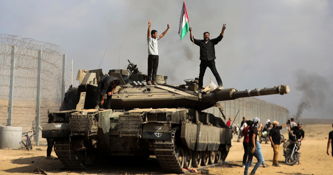 Palestinos ondean una bandera nacional y celebran junto a un taque israelí destruido en la valla fronteriza que separa la Franja de Gaza de Israel, al este de Khan Younis, el 7 de octubre de 2023. Foto: Yousef Masoud, AP