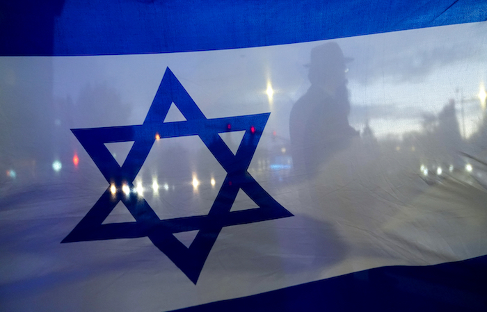 La silueta de un manifestante que cruza la calle se ve tras una bandera de Israel durante una marcha en apoyo de Israel, el lunes 9 de octubre de 2023 en Bellevue, Washington.