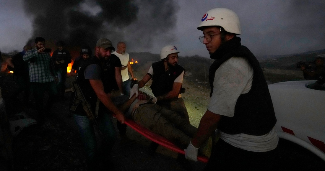 Trabajadores de protección civil y un agente de seguridad libanés cargan a un periodista que resultó herido por la caída de un proyectil israelí en Alma al-Shaab, en el sur de Líbano, el viernes 13 de octubre de 2023. Foto: Hassan Ammar, AP