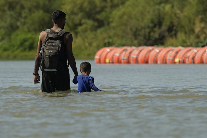 Migrantes caminan hacia unas boyas colocadas por Estados Unidos como una especie de muro flotante en el Río Bravo, el martes 1 de agosto de 2023, en Eagle Pass, Texas.