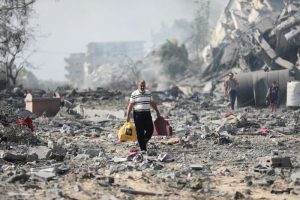 Palestinos caminan el viernes 20 de octubre de 2023 junto a edificios destruidos en un bombardeo israelí sobre al-Zahra, en las afueras de la Ciudad de Gaza.