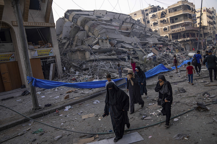 Palestinos caminan junto a un edificio en ruinas tras un ataque aéreo palestino en Ciudad de Gaza, el sábado 8 de octubre de 2023.