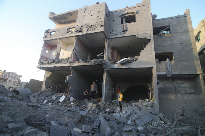 Palestinos de pie junto a un edificio destruido en un ataque aéreo israelí en la frontera de Rafah, en la Franja de Gaza, el lunes 16 de octubre de 2023.