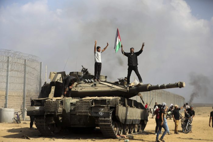 Palestinos ondean una bandera nacional y celebran junto a un taque israelí destruido en la valla fronteriza que separa la Franja de Gaza de Israel, al este de Khan Younis, el 7 de octubre de 2023.