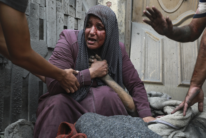 Una mujer palestina herida llora mientras sostiene la mano de su familiar muerto ante su casa tras ataques israelíes que golpearon su vecindario en Ciudad de Gaza, el lunes 23 de octubre de 2023.