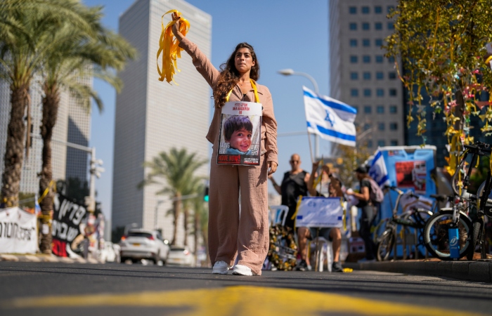 Una mujer, con la fotografía de un niño que fue tomado como rehén durante el ataque sin precedentes de Hamás en Israel, entrega listones amarillos a los automovilistas en el centro de Tel Aviv, Israel, el miércoles 25 de octubre de 2023. 