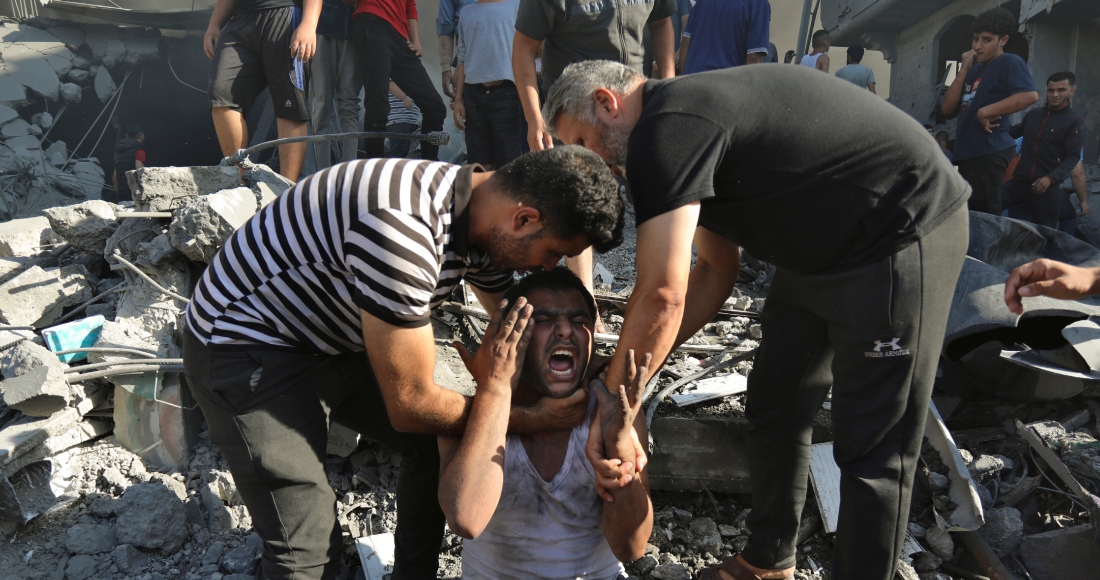 Un hombre que carga a un niño pasa encima de los cuerpos de palestinos muertos y heridos que yacen en el suelo tras un ataque aéreo israelí frente a la entrada del hospital Al Shifa, el viernes 3 de noviembre de 2023, en la Ciudad de Gaza.