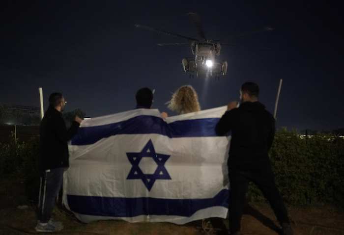 Gente sosteniendo una bandera israelí mira la llegada de un helicóptero que transporta a rehenes israelíes liberados por Hamás en el Centro Médico Sheba en Ramat Gan, Israel, el martes 28 de noviembre de 2023.