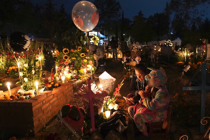 La gente se sienta alrededor de la tumba de un niño en el cementerio de San Gregorio Atlapulco durante las festividades del Día de Muertos en las afueras de la Ciudad de México, la madrugada del miércoles 1 de noviembre de 2023.