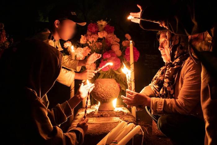 La gente sostiene velas sobre una tumba decorada con flores en un cementerio en Atzompa, México, el martes 31 de octubre de 2023 por la noche.