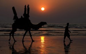 Se recorta la silueta de un hombre paquistaní y su camello en el último atardecer de 2023 en la playa de Clifton en Karachi, Pakistán, el domingo 31 de diciembre de 2023.