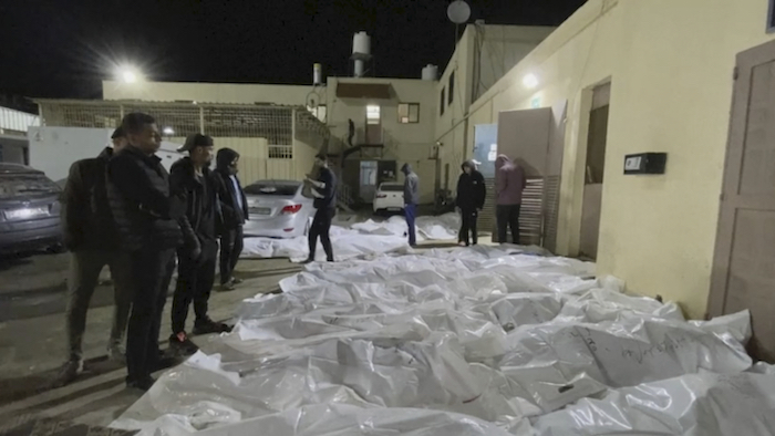 En esta imagen tomada de un video, gente mira algunos de los cuerpos llegados al hospital de Al Aqsa en Deir el Balah, Franja de Gaza, la noche del 24 de diciembre de 2023 después de tres ataques aéreos en el centro de Gaza.