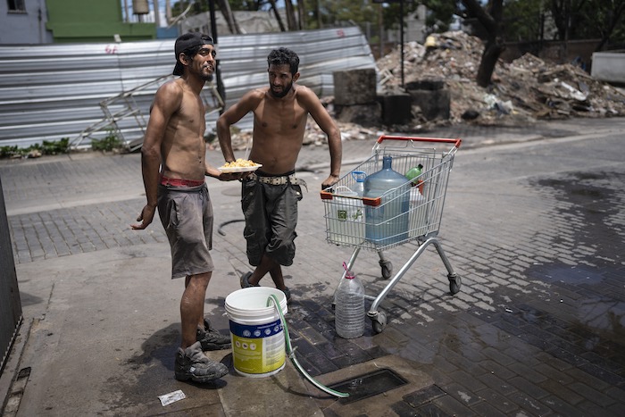 Nicolás Gonzáles, a la izquierda, y Maxi Suárez rellenan recipientes de agua de una toma de agua de la calle después de retirar un plato de comida de la Casa Comunitaria del Fondo en el barrio Padre Carlos Múgica de Buenos Aires, Argentina, el miércoles 13 de diciembre de 2023.