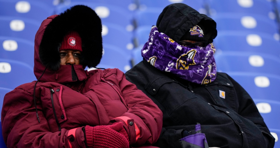 Dos personas de cobijan del frío en el partido de futbol americano entre los Ravens de Baltimore y los Texans de Houston, en Baltimore, el 20 de enero de 2024.