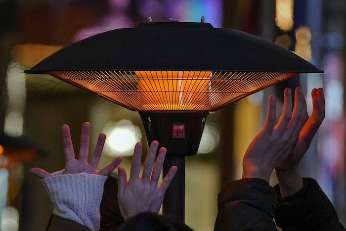 Gente tratando de calentarse las manos con un calefactor mientras esperan a su mesa ante una restaurante en un centro comercial al aire libre en Beijing, el sábado 23 de diciembre de 2023.