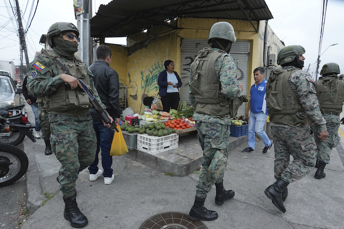 Soldados patrullan el perímetro de la prisión de Inca durante un estado de emergencia mientras un vendedor de alimentos trabaja en la acera en Quito, Ecuador, el martes 9 de enero de 2024, tras la aparente fuga de un poderoso líder de una pandilla de la cárcel.