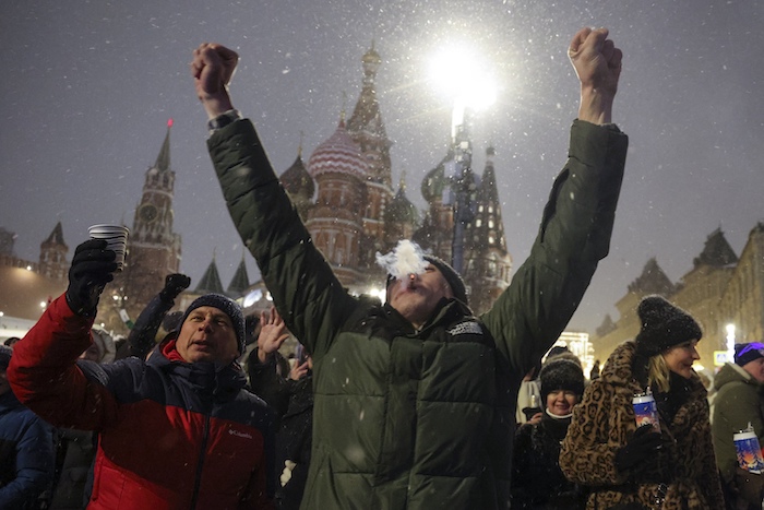 Un hombre en medio de una multitud alza los brazos cerca de la Plaza Roja, con la catedral de San Basilio --al centro-- y la torre Spasskaya --a la izquierda-- como fondo, para festejar el Año Nuevo luego de la medianoche, el lunes 1 de enero de 2024, en Moscú, Rusia.