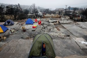 Un hombre mira desde la tienda donde acampó para pasar la noche en el lugar donde se encontraba su casa antes de ser destruida por un incendio forestal en el barrio Villa Independencia de Viña del Mar, Chile, el martes 6 de febrero de 2024.