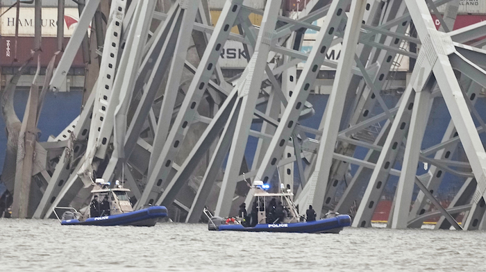 Barcos de la policía trabajan alrededor de un carguero atrapado bajo parte de la estructura del puente Francis Scott Key, el miércoles 27 de marzo de 2024, en Baltimore, un día después de que el carguero chocó contra una columna del puente y causó su derrumbe.