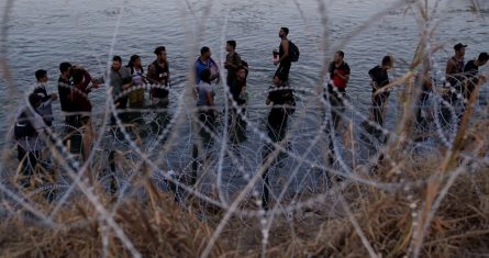 Migrantes esperan para trepar por encima del alambre de púas después de cruzar el Río Bravo y entrar en Estados Unidos desde México, el 23 de septiembre de 2023, en Eagle Pass, Texas.