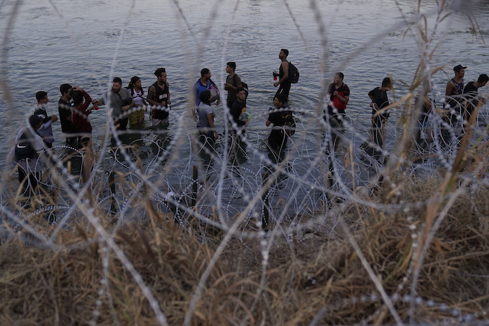 Migrantes esperan para trepar por encima del alambre de púas después de cruzar el Río Bravo y entrar en Estados Unidos desde México, el 23 de septiembre de 2023, en Eagle Pass, Texas.