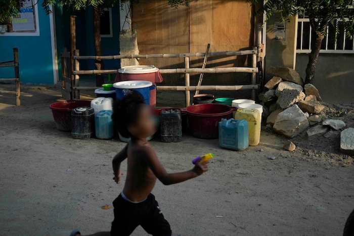 Un niño corre por delante de varios recipientes al frente de una casa, esperando el camión que lleva agua para llenarlos, en el barrio de Los Polvorines de Piura, Perú, el jueves 29 de febrero de 2024.