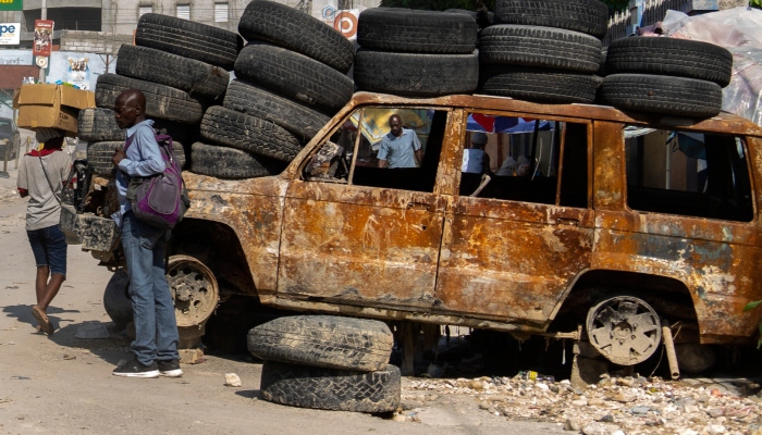 Gente pasa junto a neumáticos y un vehículo quemado utilizado para cortar una calle en la zona de Canapé Vert, Puerto Príncipe, Haití, el lunes 22 de abril de 2024. 