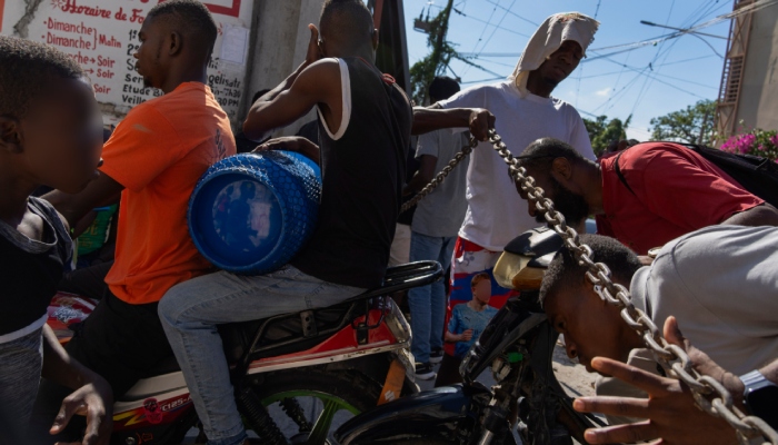 Un hombre levanta una cadena utilizada como barricada para que los vecinos pasen al vecindario, mientras preparan una puerta de metal para protegerse de las pandillas en el vecindario de Petion-Ville, Puerto Príncipe, el sábado 20 de abril de 2024. 