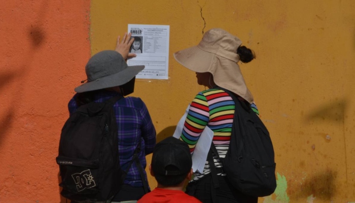 Mujeres colocan fichas de búsqueda de Javier en una pared. Continúan esfuerzos para localizar al niño indígena y jornalero. 