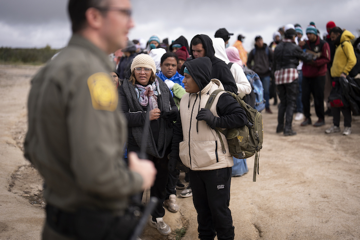 La peruana Julia Paredes, en el centro con un gorro blanco, escucha las instrucciones de un agente de la Patrulla Fronteriza con otros solicitantes de asilo mientras esperan a ser procesados tras cruzar la cercana frontera con México, el jueves 25 de abril de 2024 en Boulevard, California.