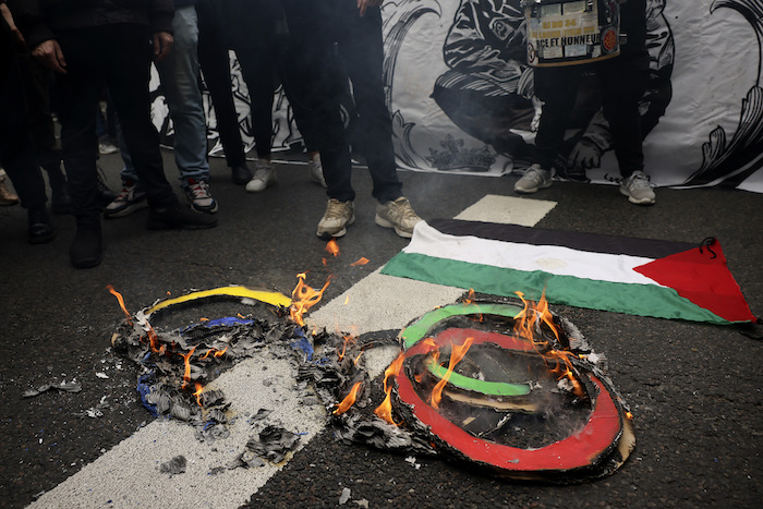 Manifestantes queman los anillos olímpicos en el pavimento al lado de una bandera palestina en la marcha del Día del Trabajo el miércoles 1 de mayo de 2024 en París.