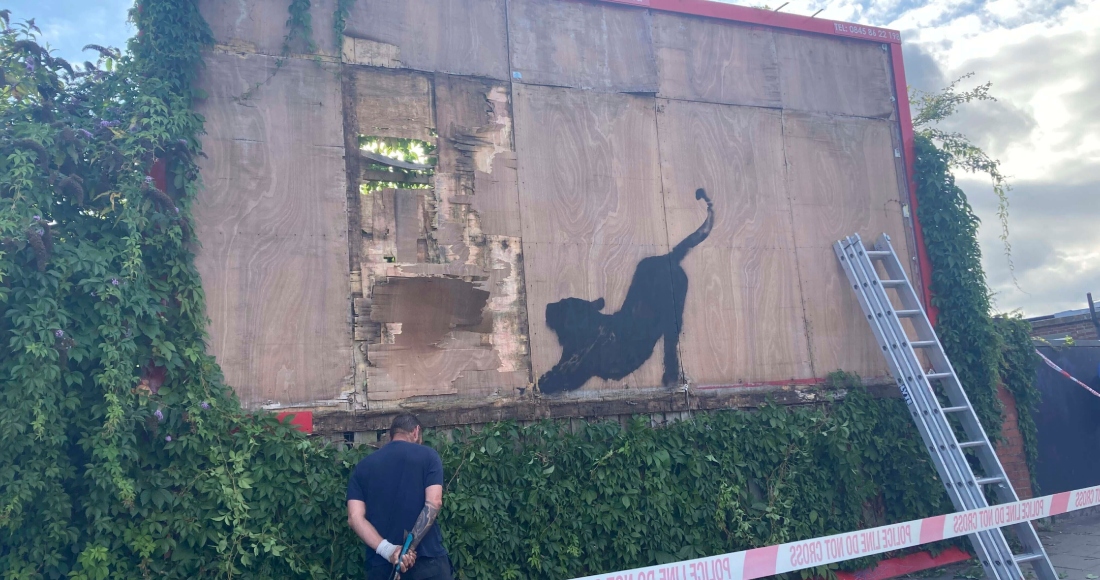 Contratistas comienzan a desmantelar una mampara con una nueva obra de arte de Banksy que representa un felino estirándose en Cricklewood, noroeste de Londres, el sábado 10 de agosto de 2024. 