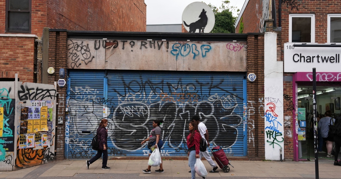 Personas caminan pasa junto a una nueva obra de arte que representa un lobo aullando creada por Banksy sobre una antena parabólica colocada en el techo de una tienda en Peckham, al sur de Londres, el jueves 8 de agosto de 2024. 