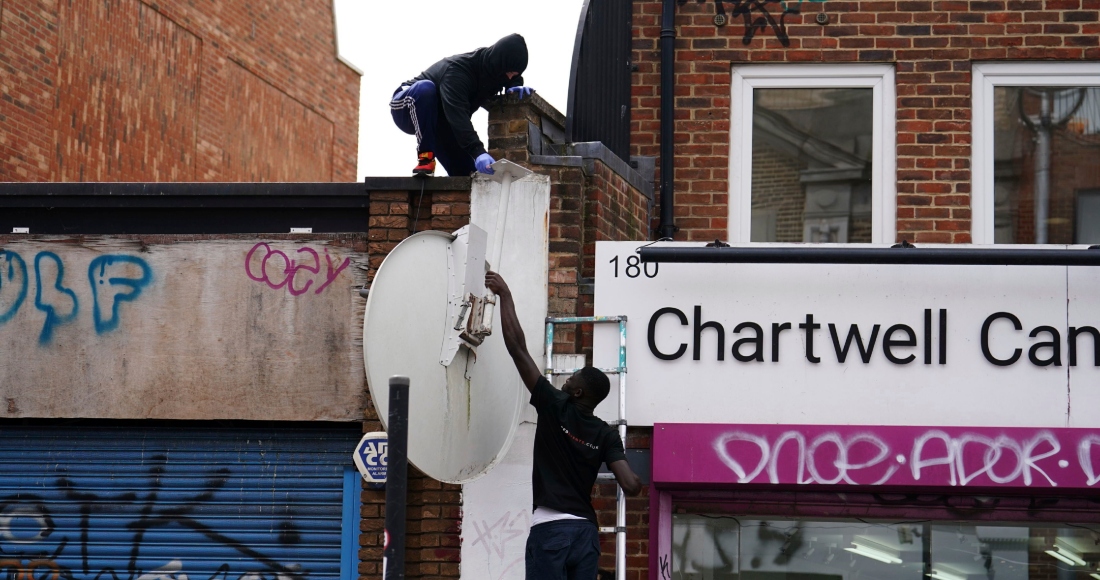 Personas retiran una nueva obra de arte de Banksy, que representa un lobo aullando pintado en una antena parabólica que se colocó en el techo de una tienda en Peckham, al sur de Londres, el jueves 8 de agosto de 2024. 