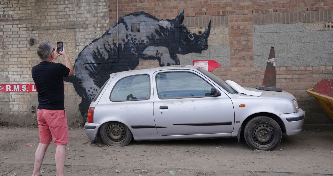 Un hombre fotografía una nueva obra de arte de Banksy, que representa un rinoceronte que parece subirse a un automóvil, la octava obra de arte de su colección de temática animal, en Westmoor Street en Charlton, sureste de Londres, el lunes 12 de agosto de 2024.