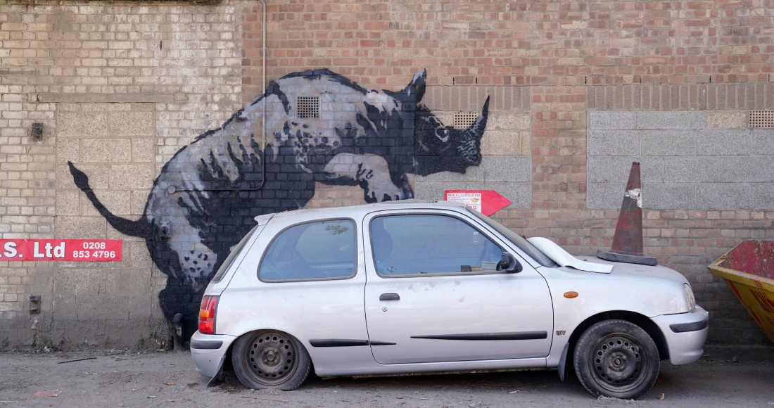 Personas caminan pasa junto a una nueva obra de arte que representa un lobo aullando creada por Banksy sobre una antena parabólica colocada en el techo de una tienda en Peckham, al sur de Londres, el jueves 8 de agosto de 2024.