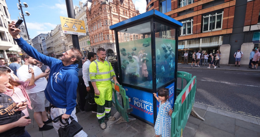 Un hombre se toma una selfie furente a una obra de peces de Banksy, que apareció en una cabina de policía en la ciudad de Londres, es acordonada en Londres, el lunes 12 de agosto de 2024. 