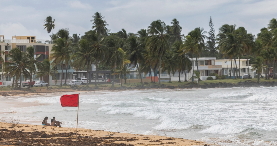 Turistas sentados en la playa La Pared mientras la tormenta tropical Ernesto pasa por Luquillo, Puerto Rico, el martes 13 de agosto de 2024.